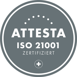A round, gray plaque with white lettering reads "ATTESTA ISO 21001 CERTIFIED." At the bottom is a plus sign; above "ATTESTA" is a row of dots and the MaxBrain seal of quality.