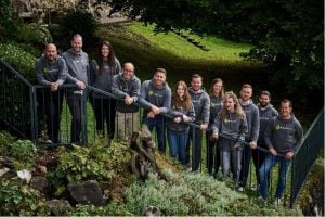 Douze personnes, toutes vêtues de sweats à capuche MaxBrain gris assortis, sont debout près d'une balustrade à l'extérieur
